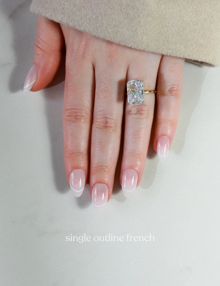 Hand wearing a diamond ring with 'single outline french' nail design on a neutral background
