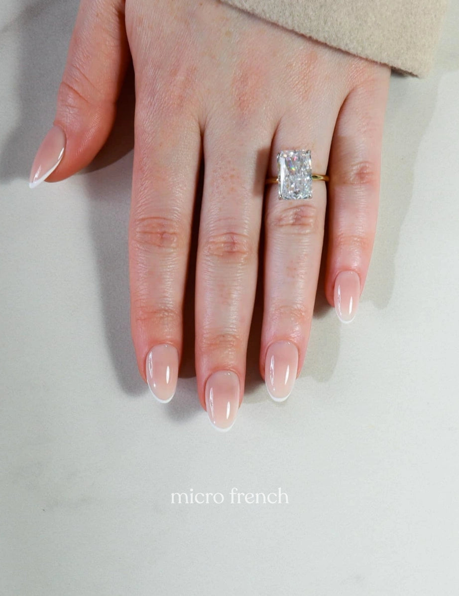 Hand wearing a diamond ring with 'micro french' text on a neutral background