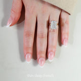 Hand wearing a diamond ring with 'thin deep french' nail design on a neutral background