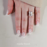 Hand wearing a diamond ring with 'regular french' nail design on a neutral background