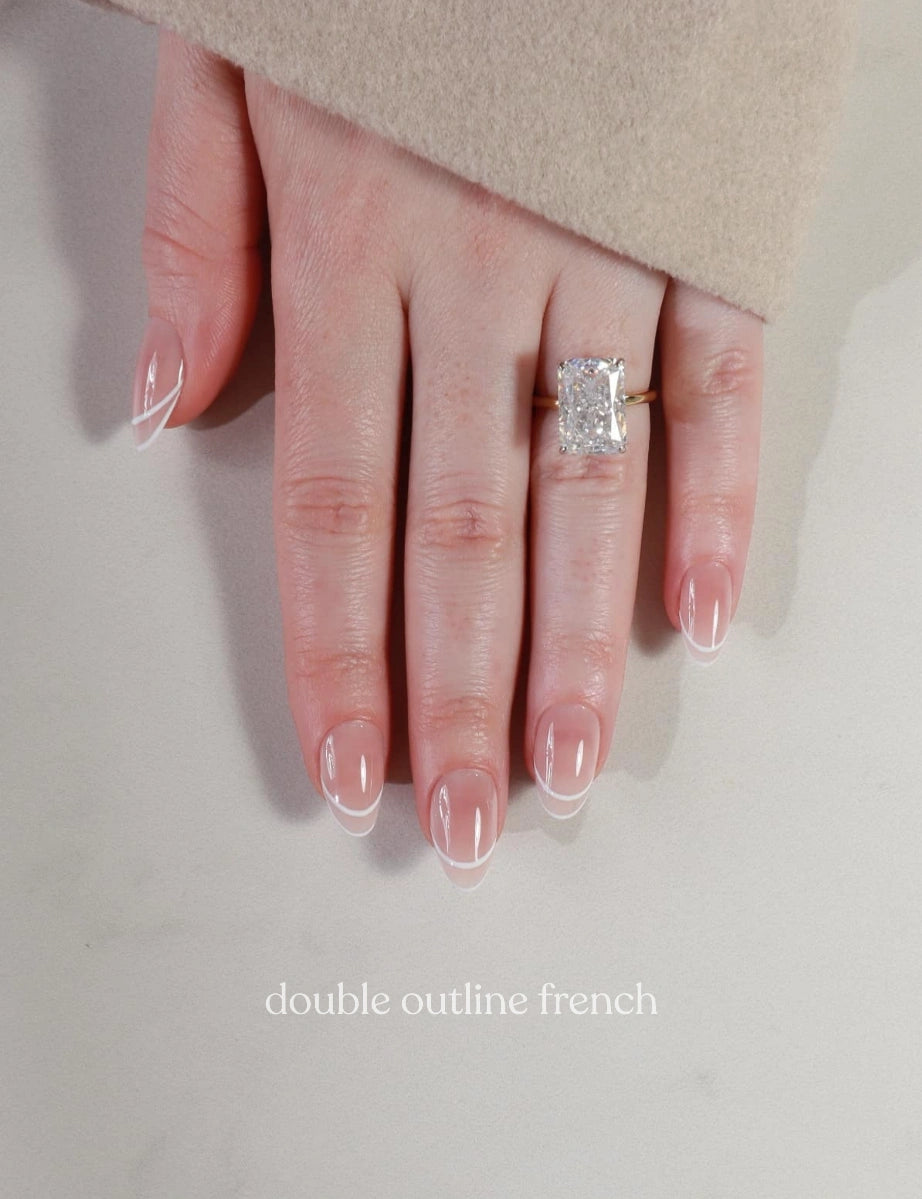Hand wearing a diamond ring with 'double outline french' nail design on a neutral background