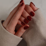 Close-up of a hand with dark red nail polish wearing a beige coat.