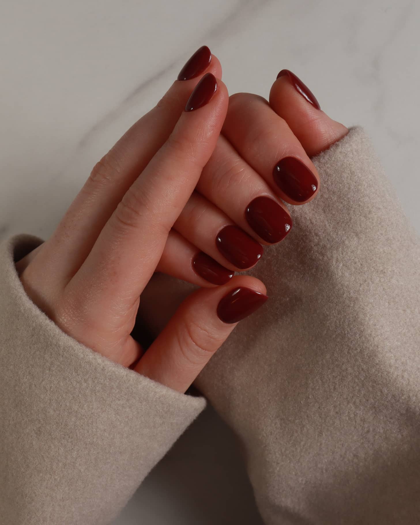 Close-up of a hand with dark red nail polish wearing a beige coat.
