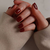 Close-up of hands with dark red nail polish wearing beige gloves.