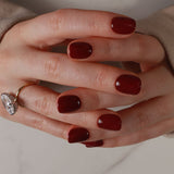 Close-up of a hand with dark red nail polish on a neutral background