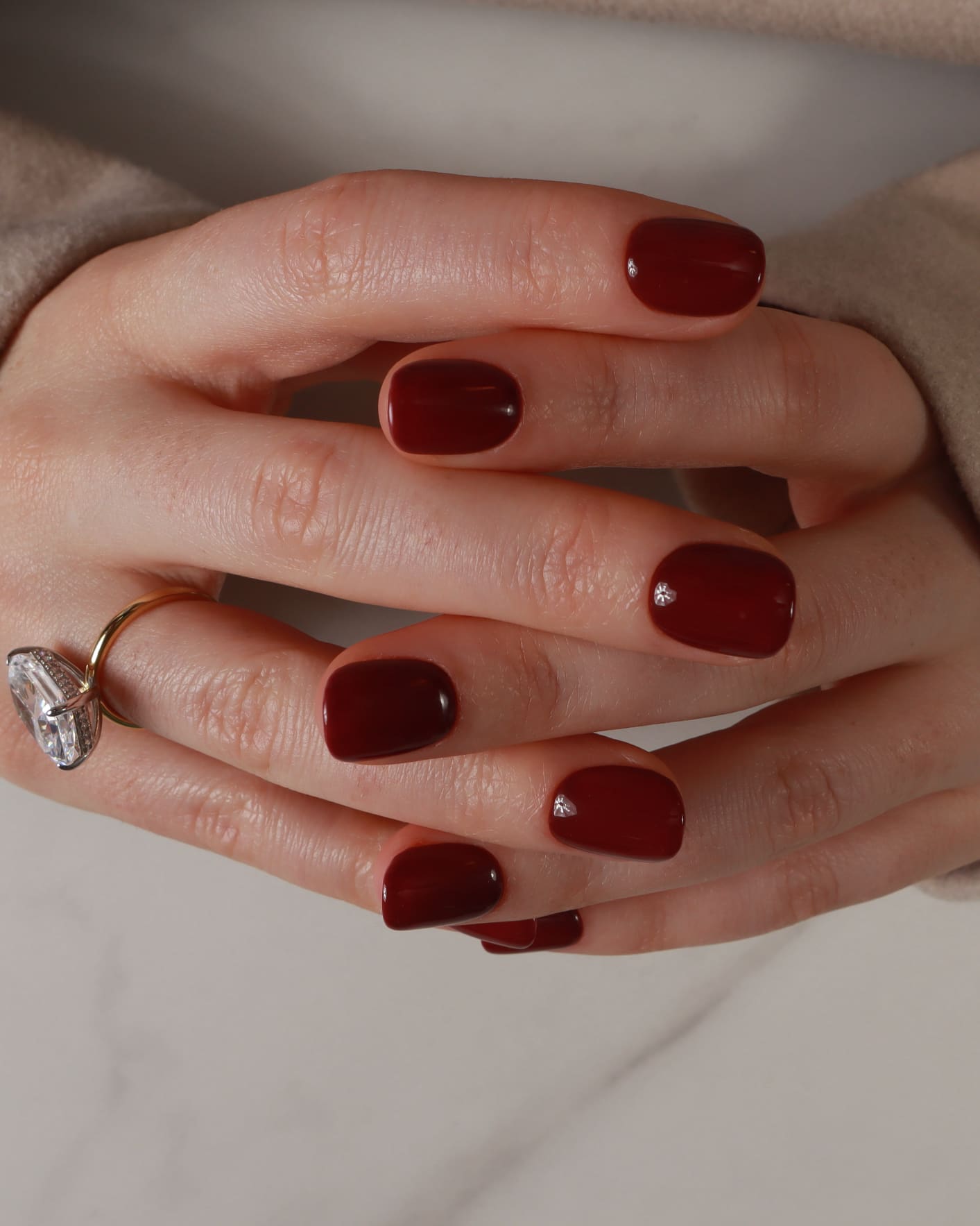Close-up of a hand with dark red nail polish on a neutral background