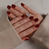 Hand with red nail polish wearing a diamond ring, wearing beige gloves on a neutral background