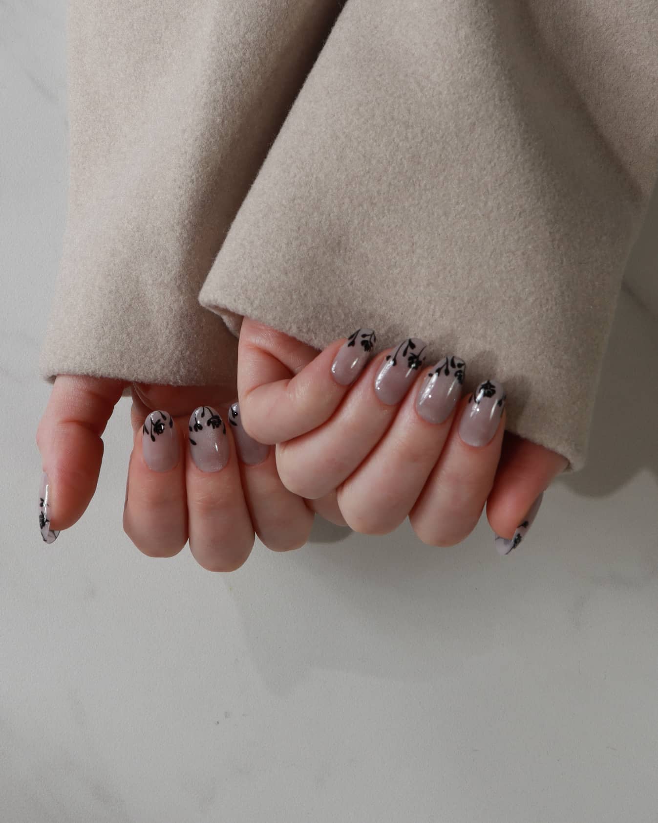Close-up of hands with stylish nail designs wearing a beige coat.