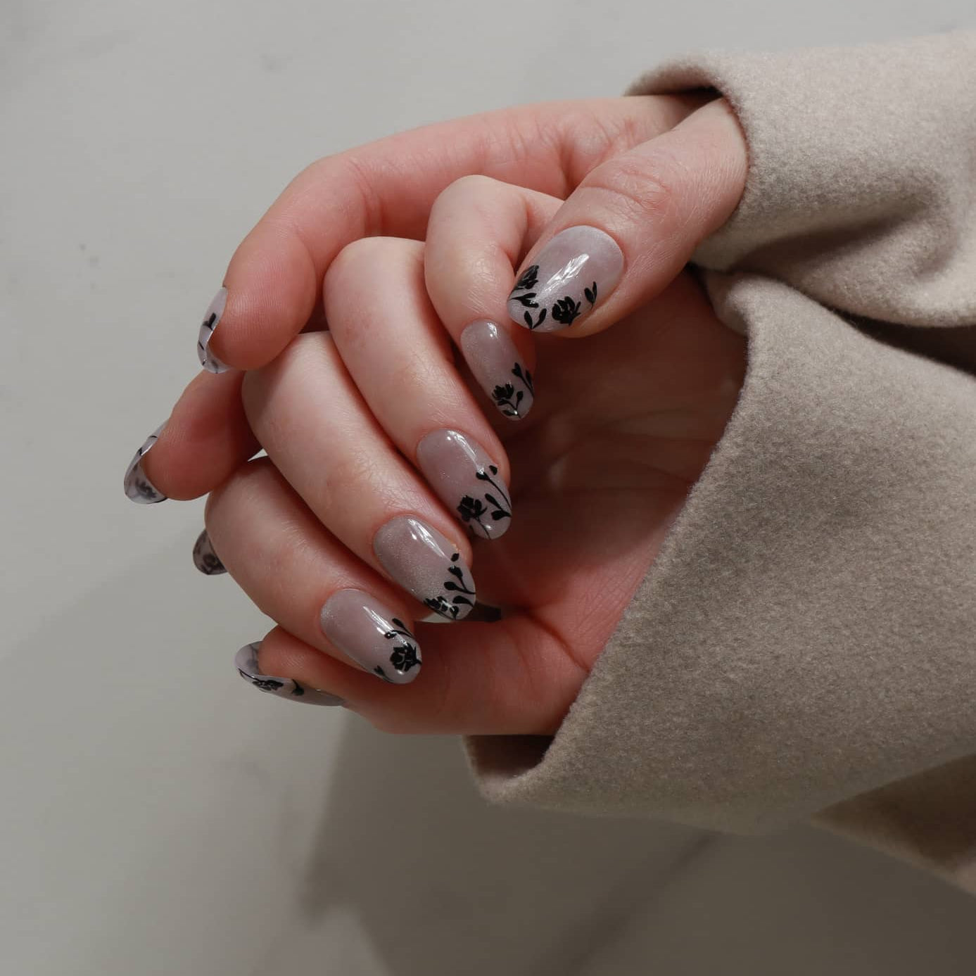 Close-up of hands with floral nail design on a neutral background