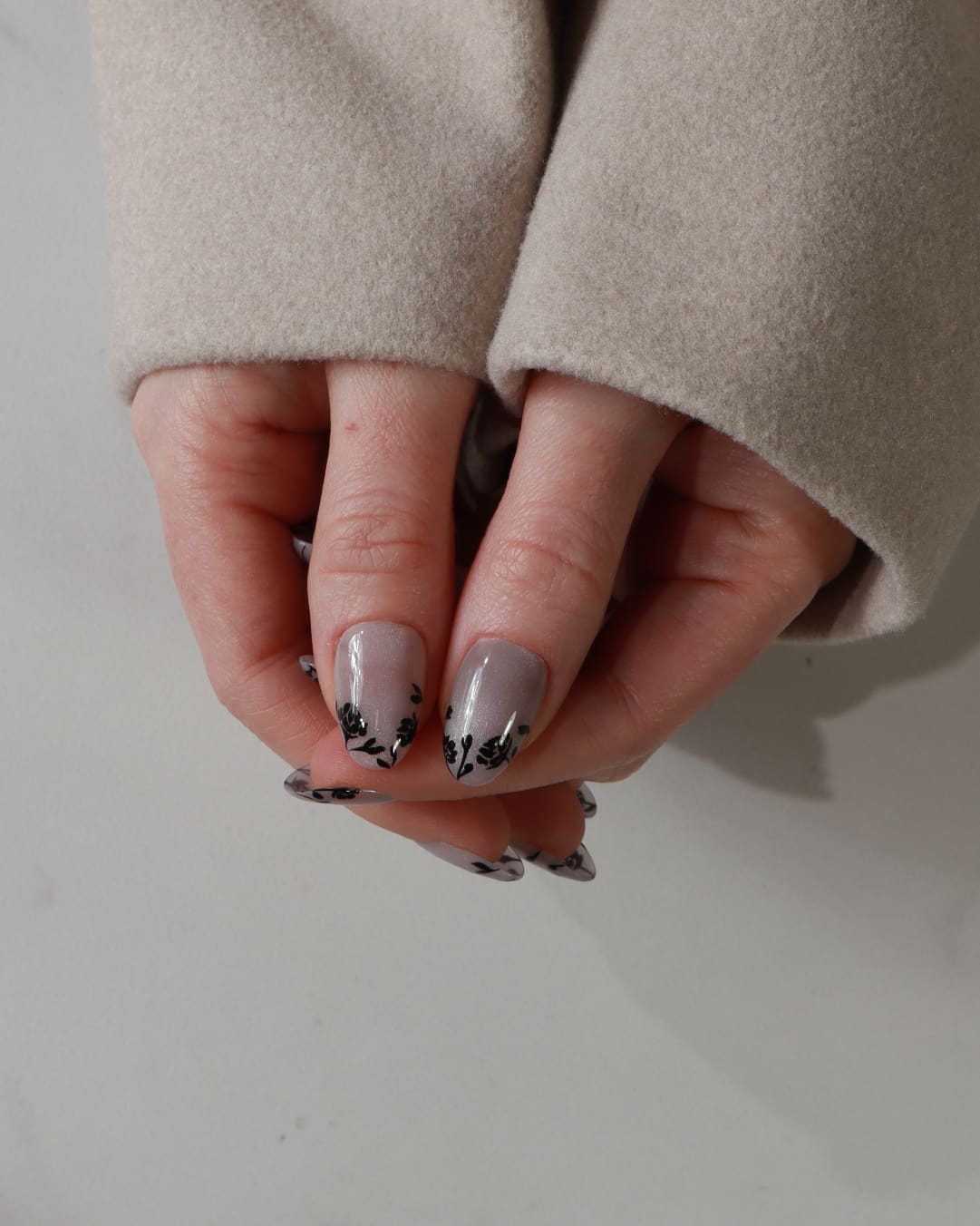Close-up of a hand with gray nail polish and black floral designs on a neutral background