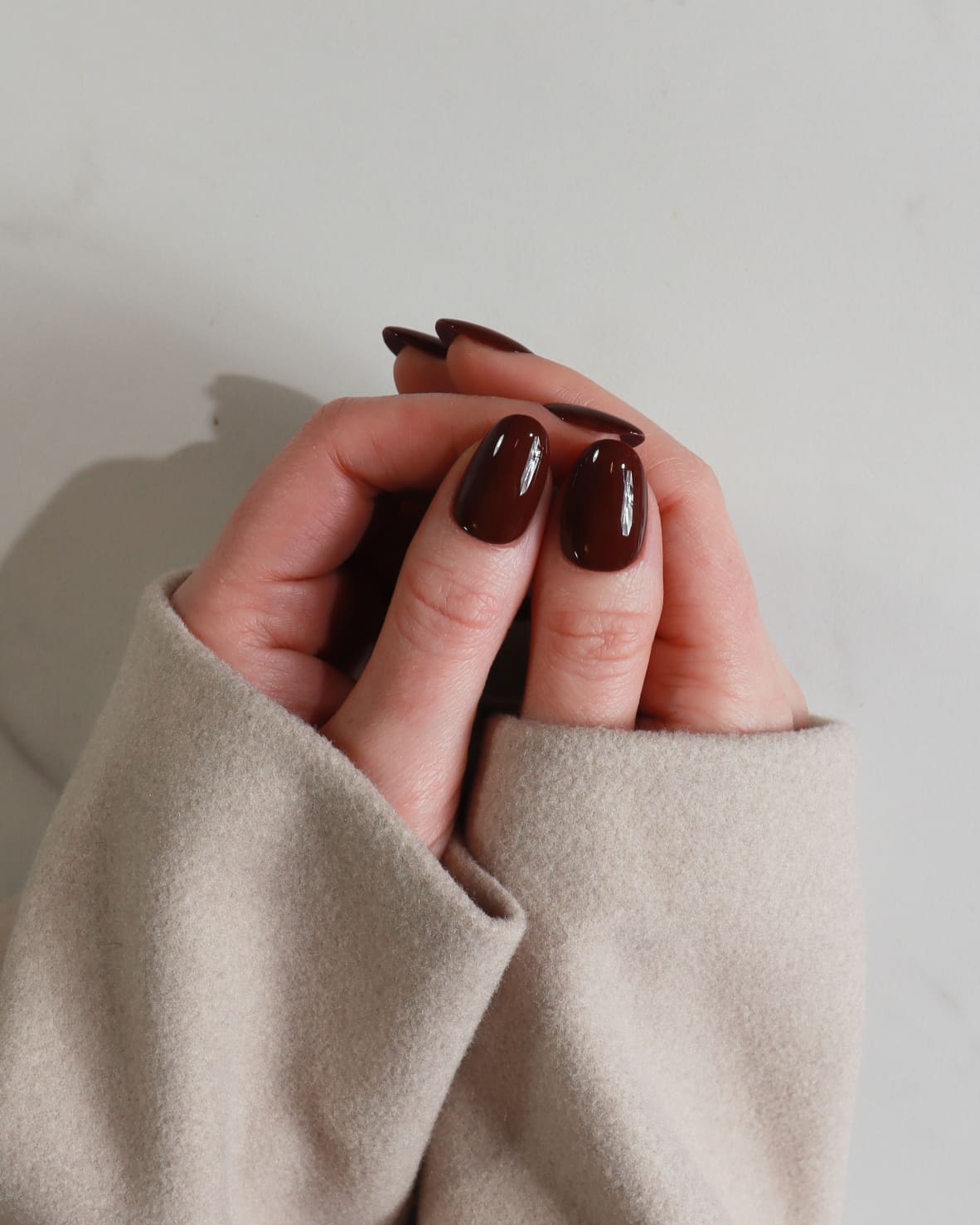Close-up of a hand with dark nail polish wearing a beige sleeve against a neutral background