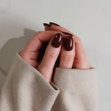 Close-up of a hand with dark nail polish wearing a beige sleeve against a neutral background