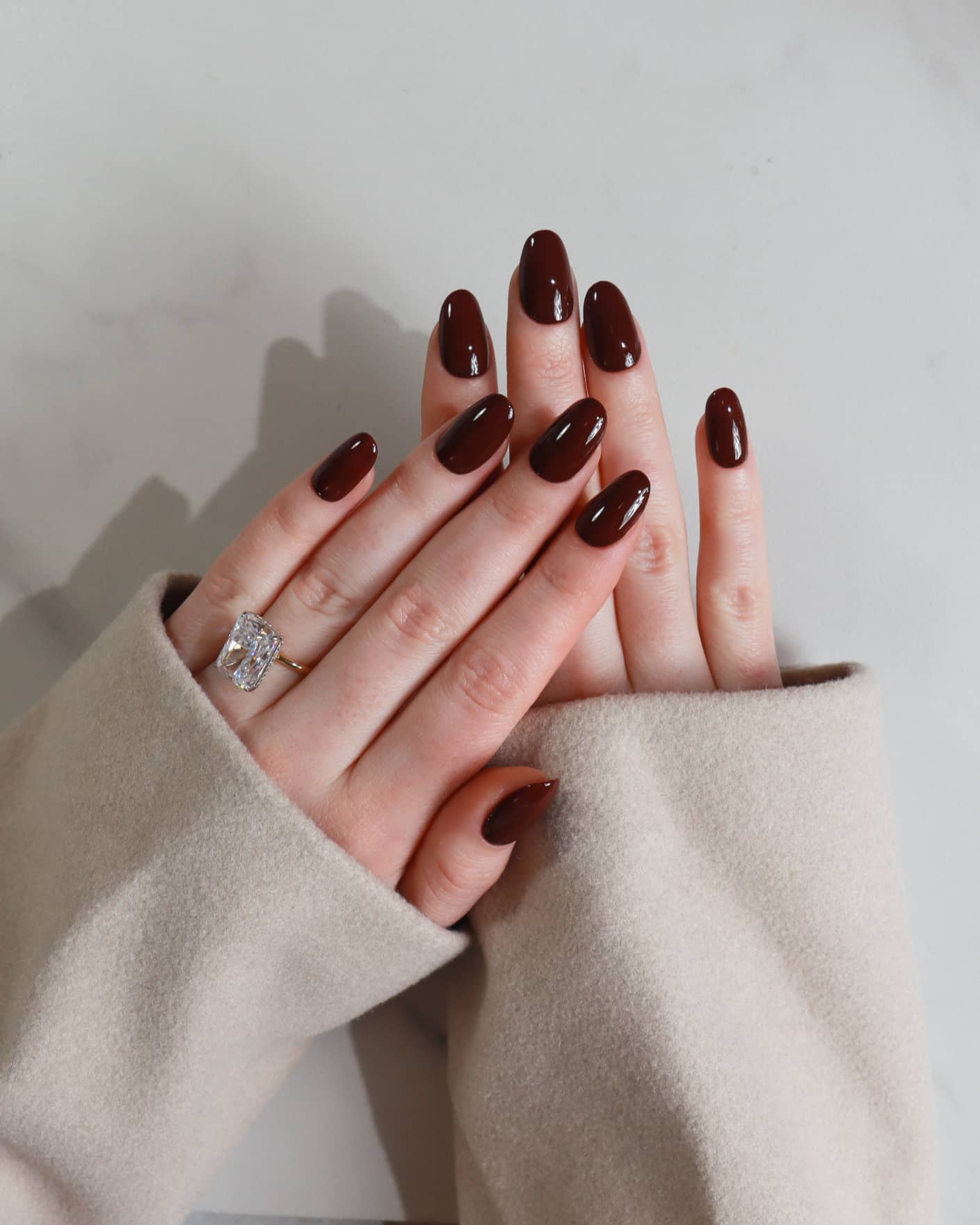 Hand with dark nail polish wearing a ring on a neutral background