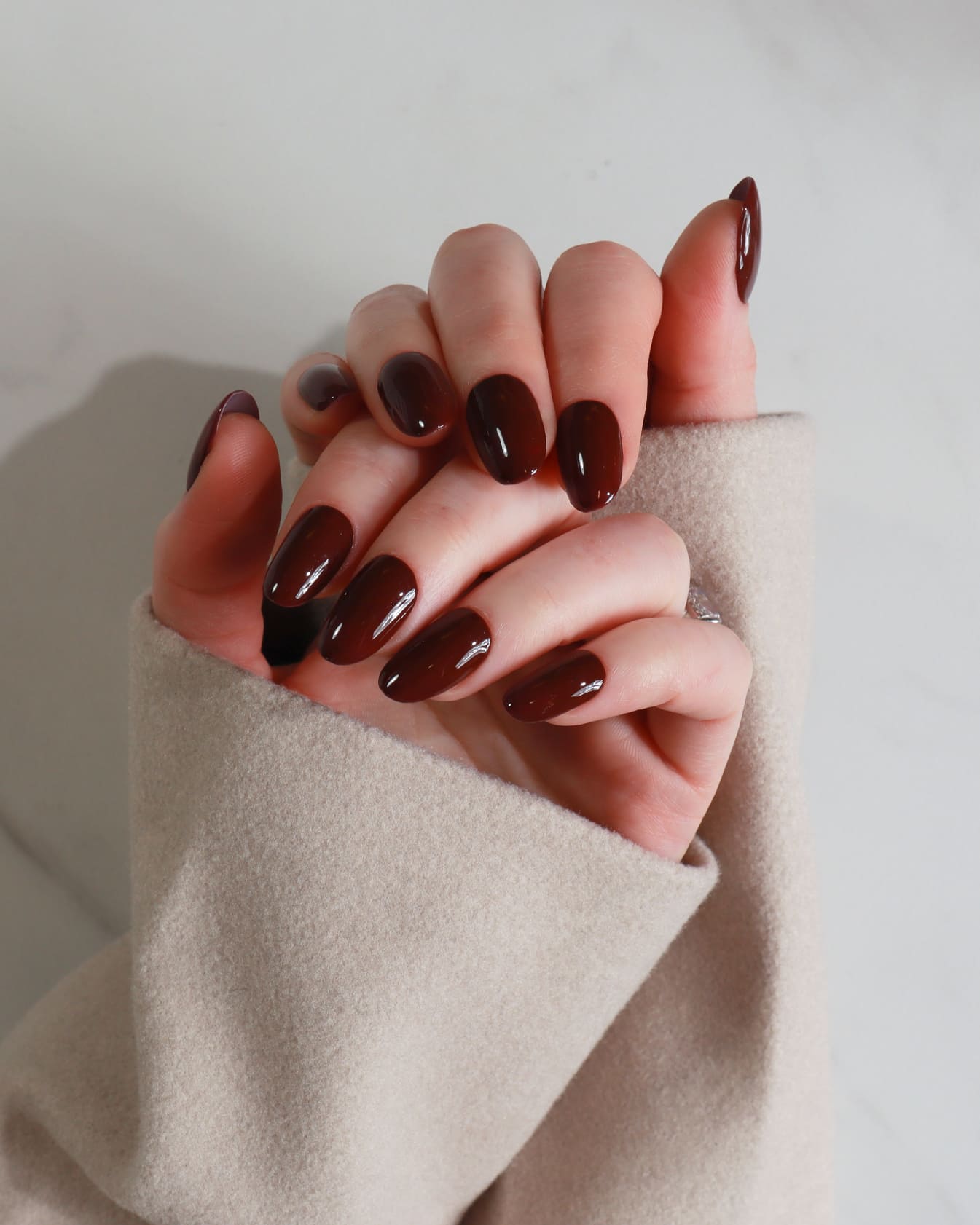 Close-up of a hand with dark nail polish wearing a beige sleeve against a neutral background