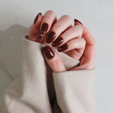 Close-up of hands with dark nail polish wearing a beige sweater against a neutral background