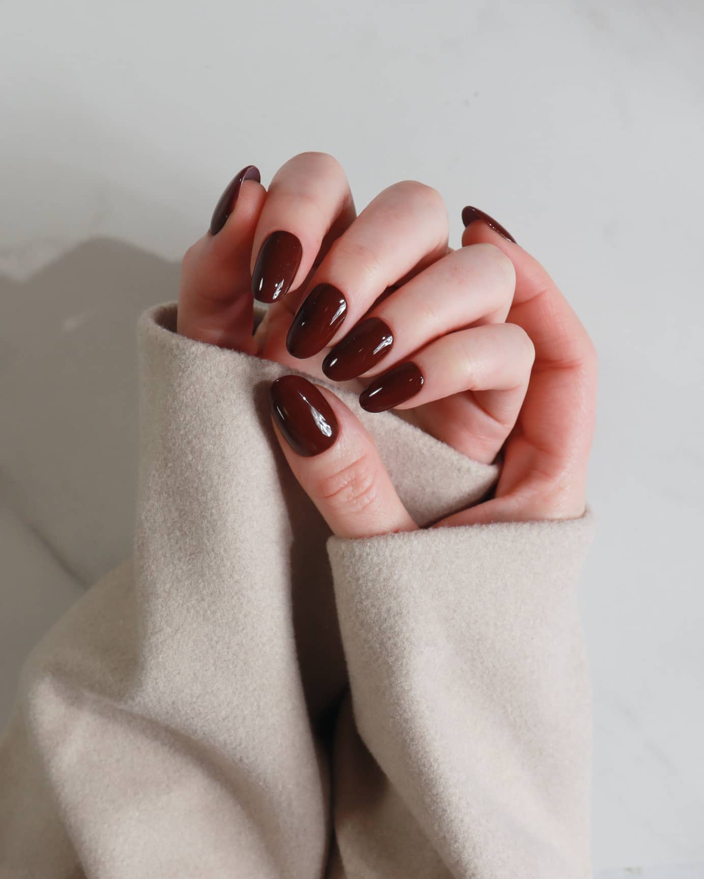 Close-up of hands with dark polish wearing a beige sweater against a neutral background