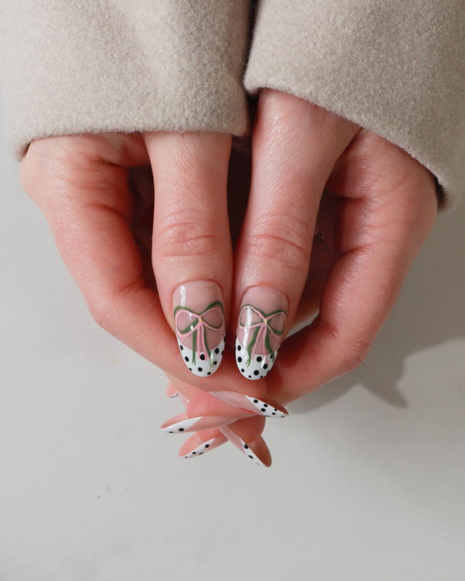 Close-up of a hand with nail art featuring polka dots and bows on a neutral background