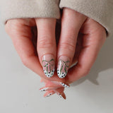 Close-up of a hand with nail art featuring polka dots and bows on a neutral background
