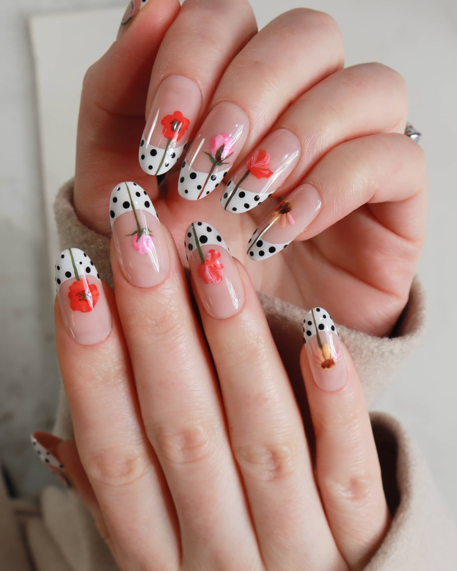 Close-up of hands with decorative nail art featuring polka dots and flowers.