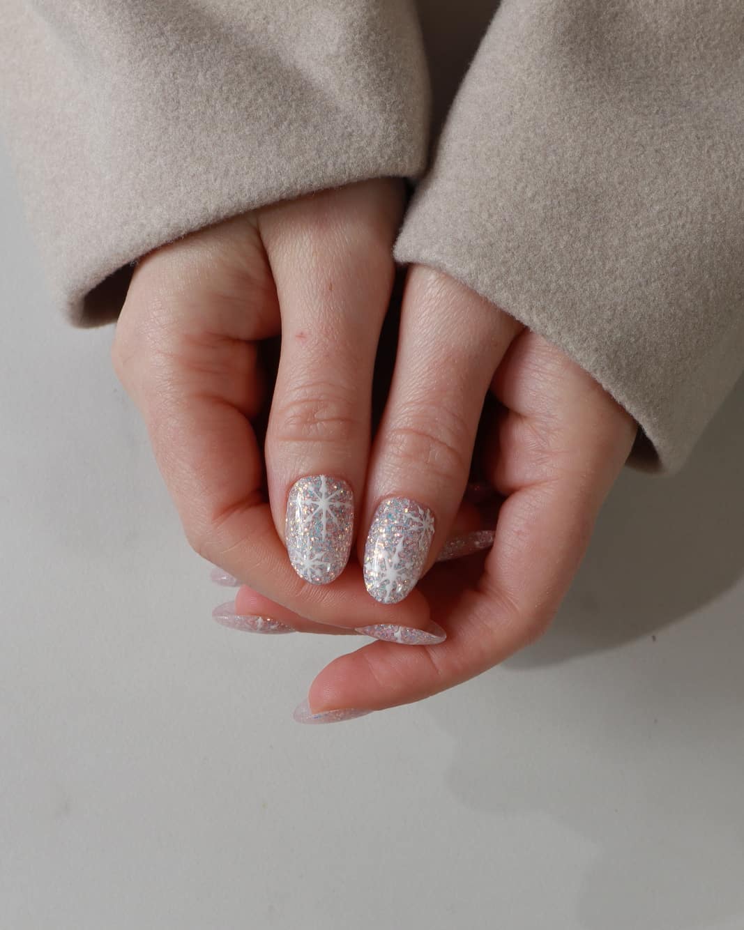 Close-up of hands with glittery gel polish on a neutral background