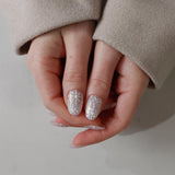 Close-up of hands with glittery gel polish on a neutral background