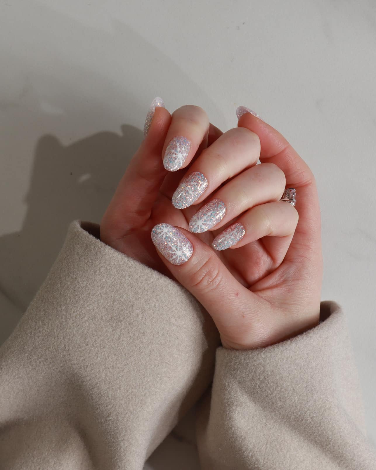 Close-up of hands with glittery gel polish against a neutral background
