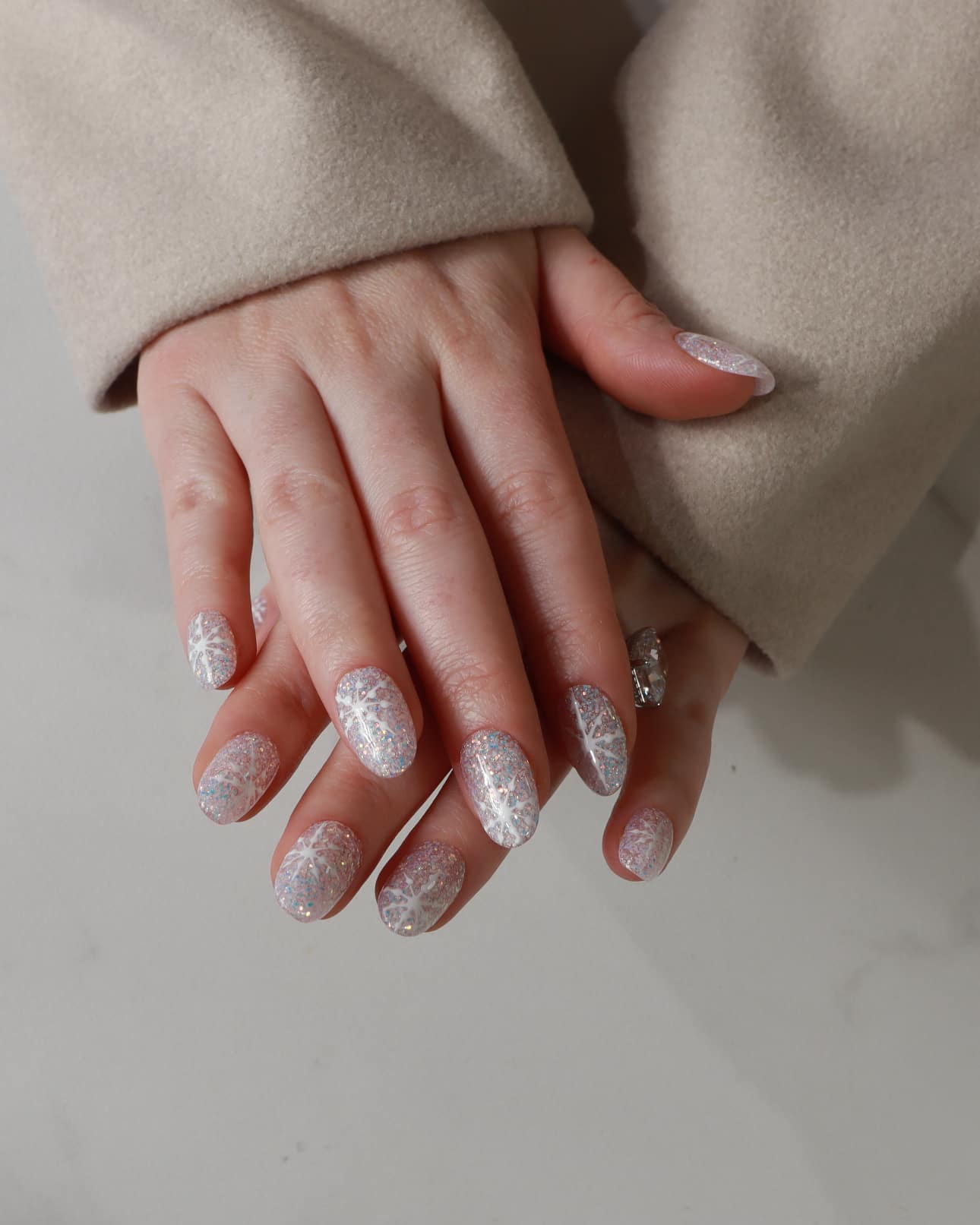Close-up of a hand with glittery gel polish wearing a beige coat.