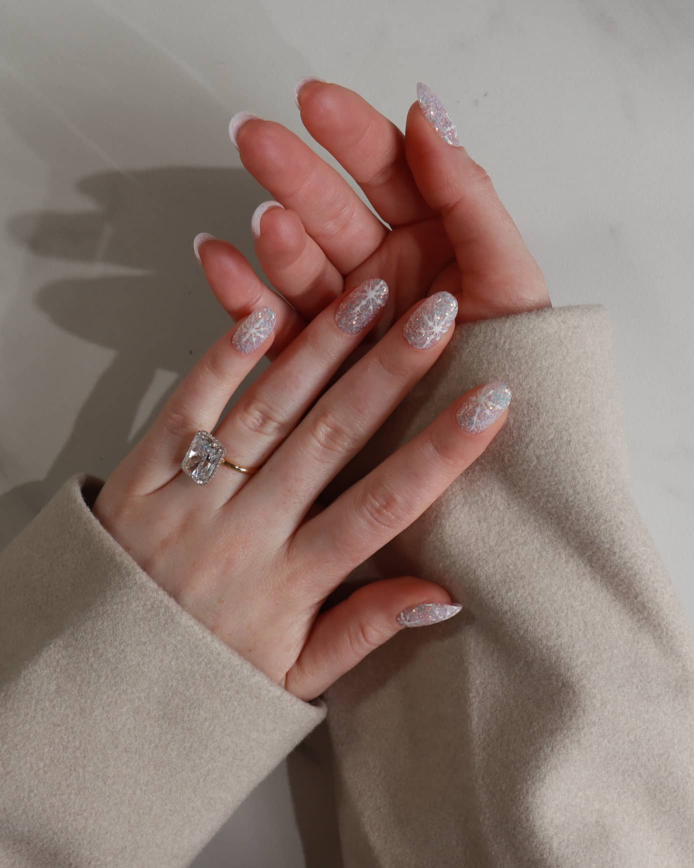 Hand with glittery gel polish wearing a ring on a neutral background
