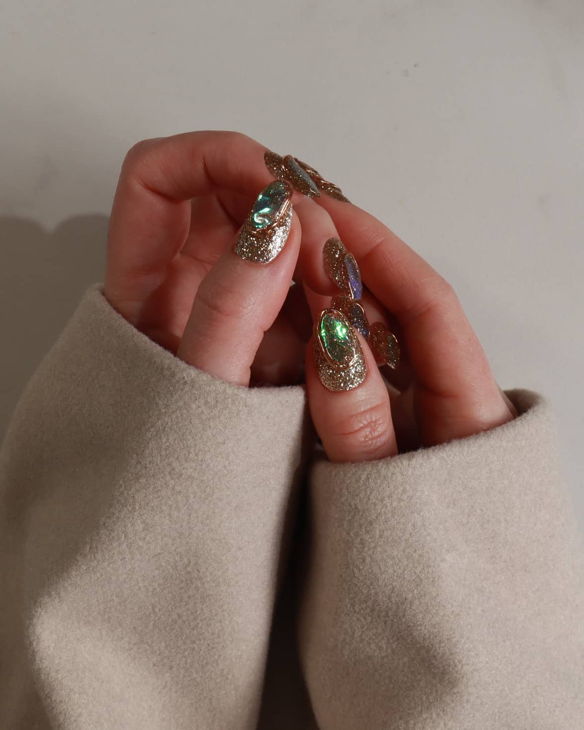 Close-up of hands wearing gold and green polish with a neutral background