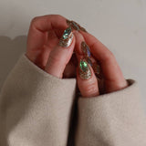 Close-up of hands wearing gold and green polish with a neutral background