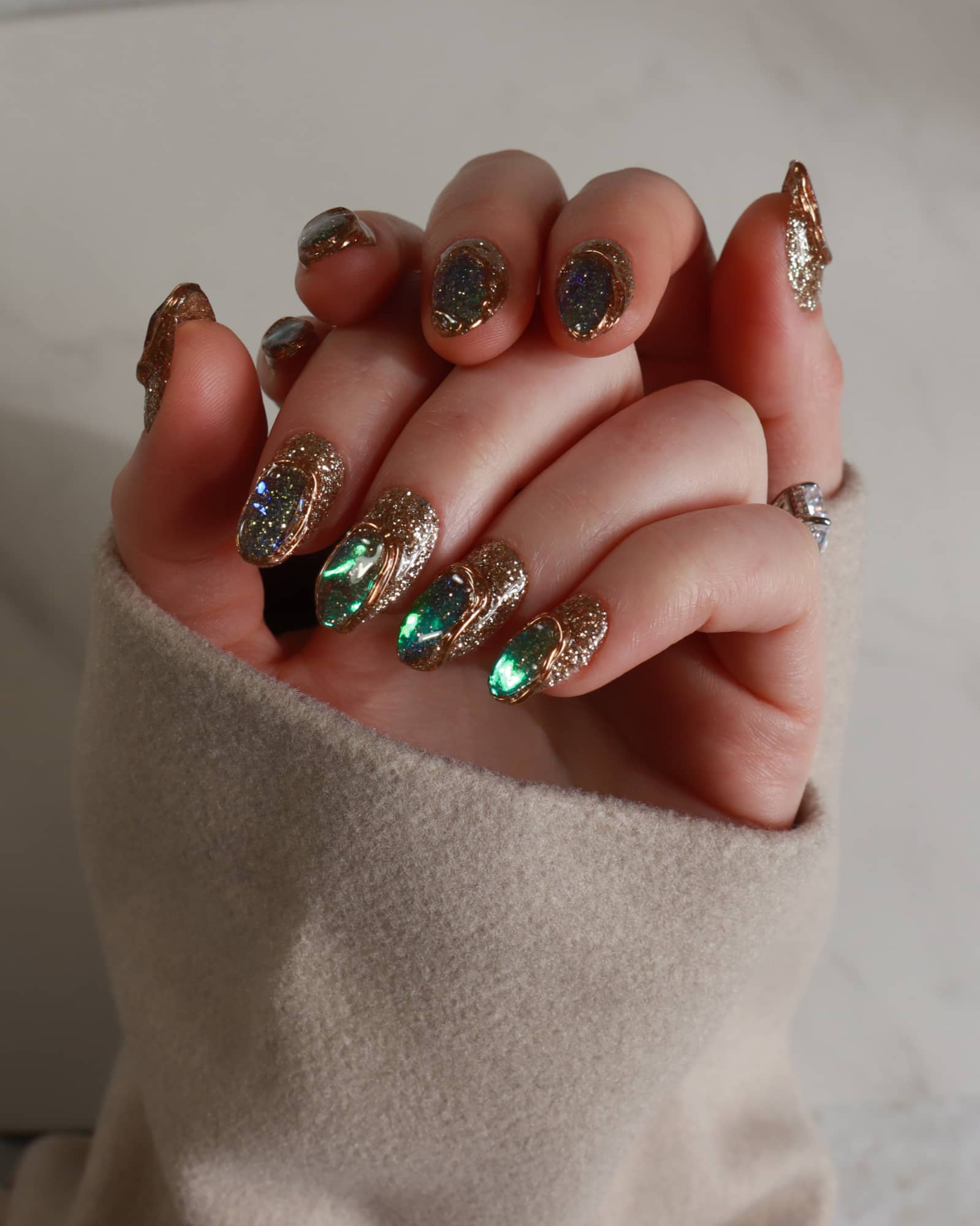 Close-up of a hand with ornate nail art wearing a beige sweater.