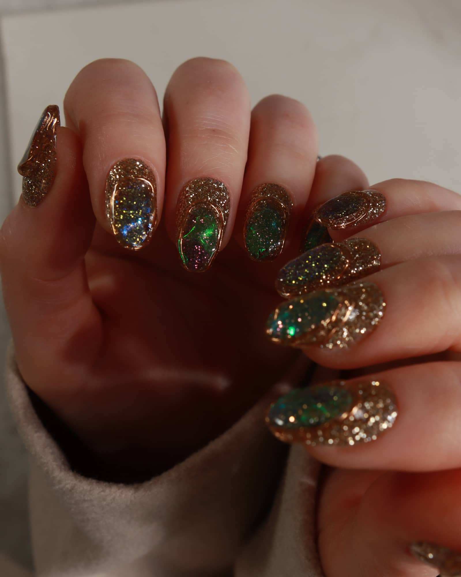 Close-up of a hand with glittery green and gold polish.