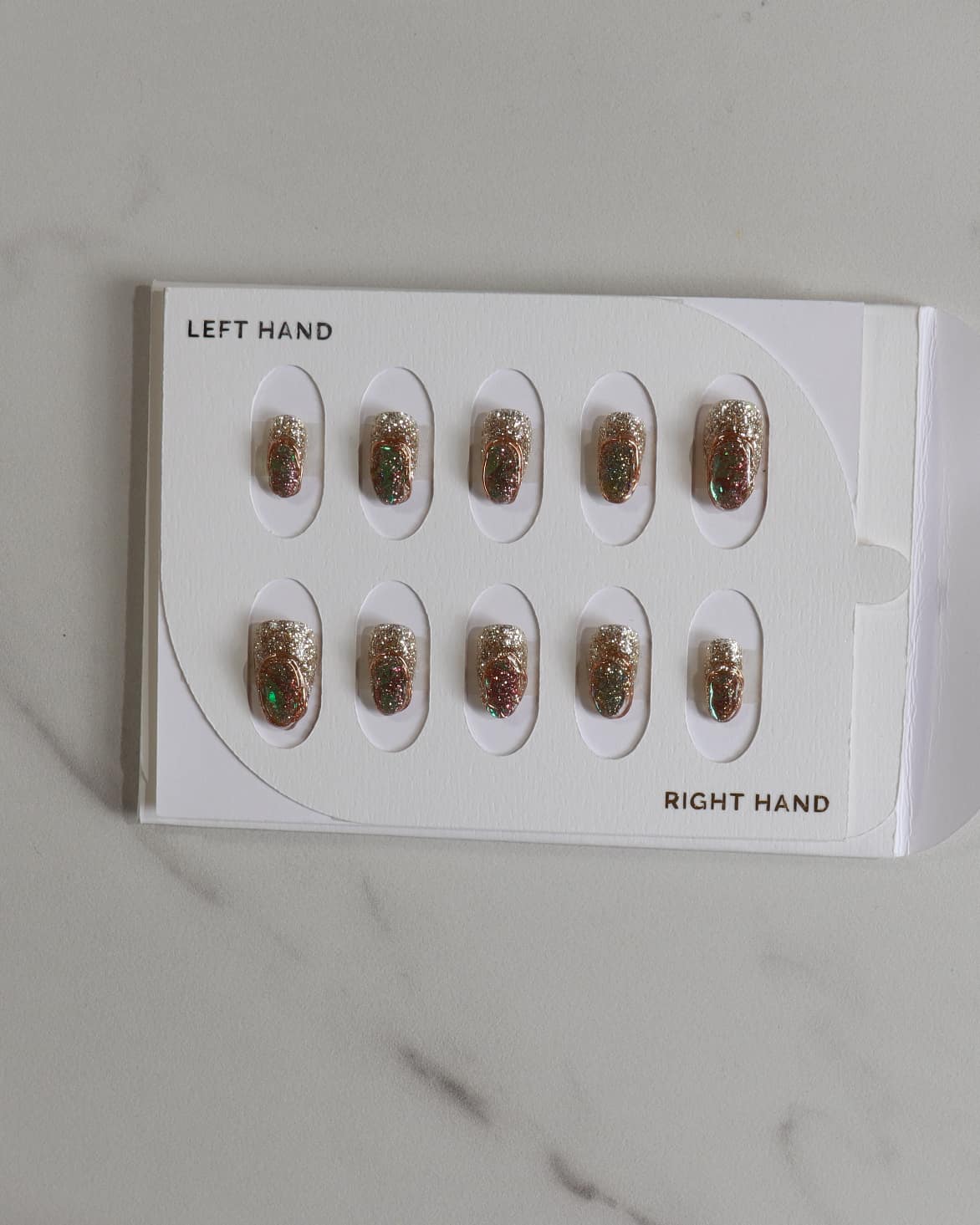 Set of gold nail art designs on a white card with 'LEFT HAND' and 'RIGHT HAND' labels on a marble surface.