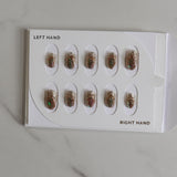 Set of gold nail art designs on a white card with 'LEFT HAND' and 'RIGHT HAND' labels on a marble surface.
