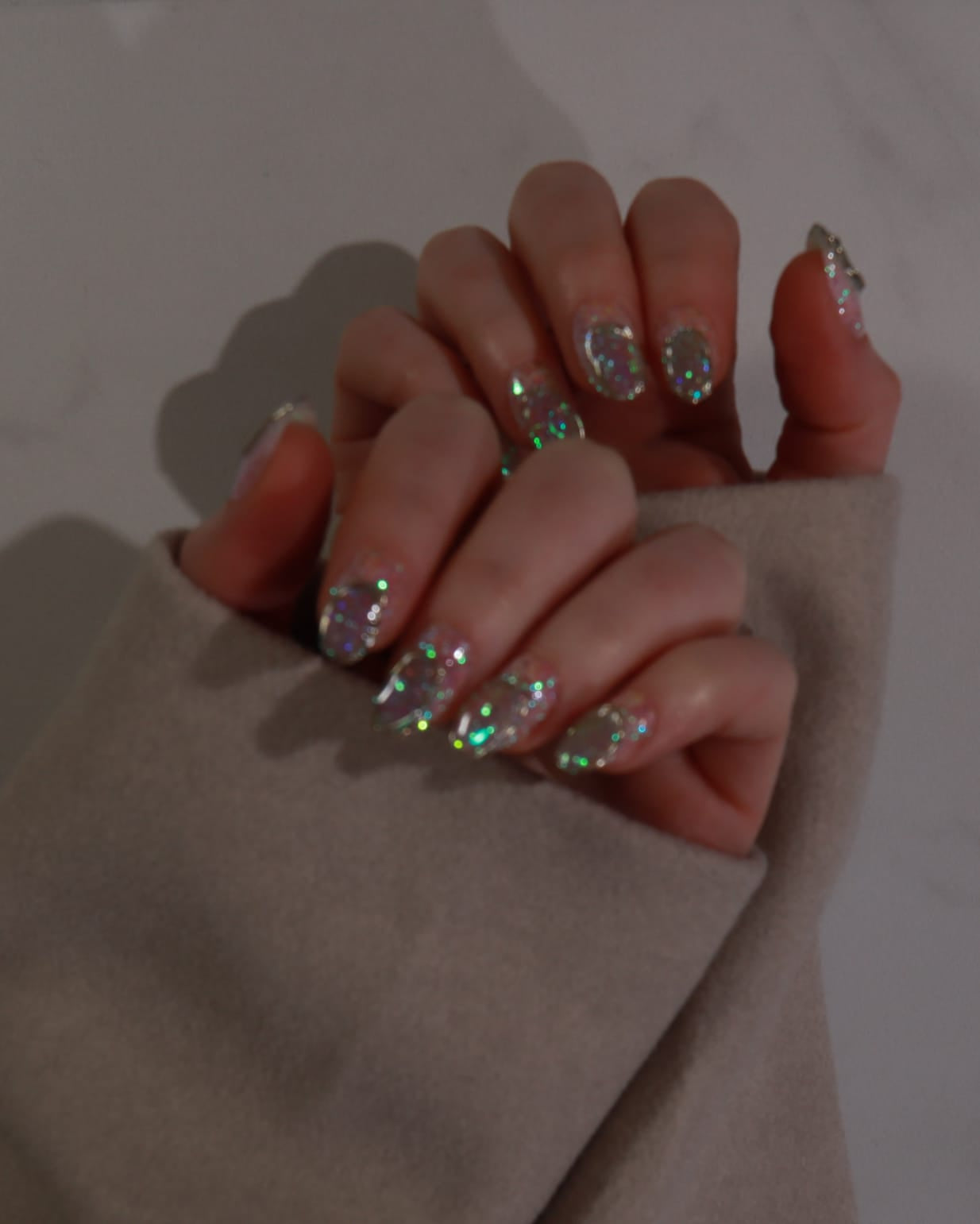 Close-up of a hand with glittery nail polish on a neutral background