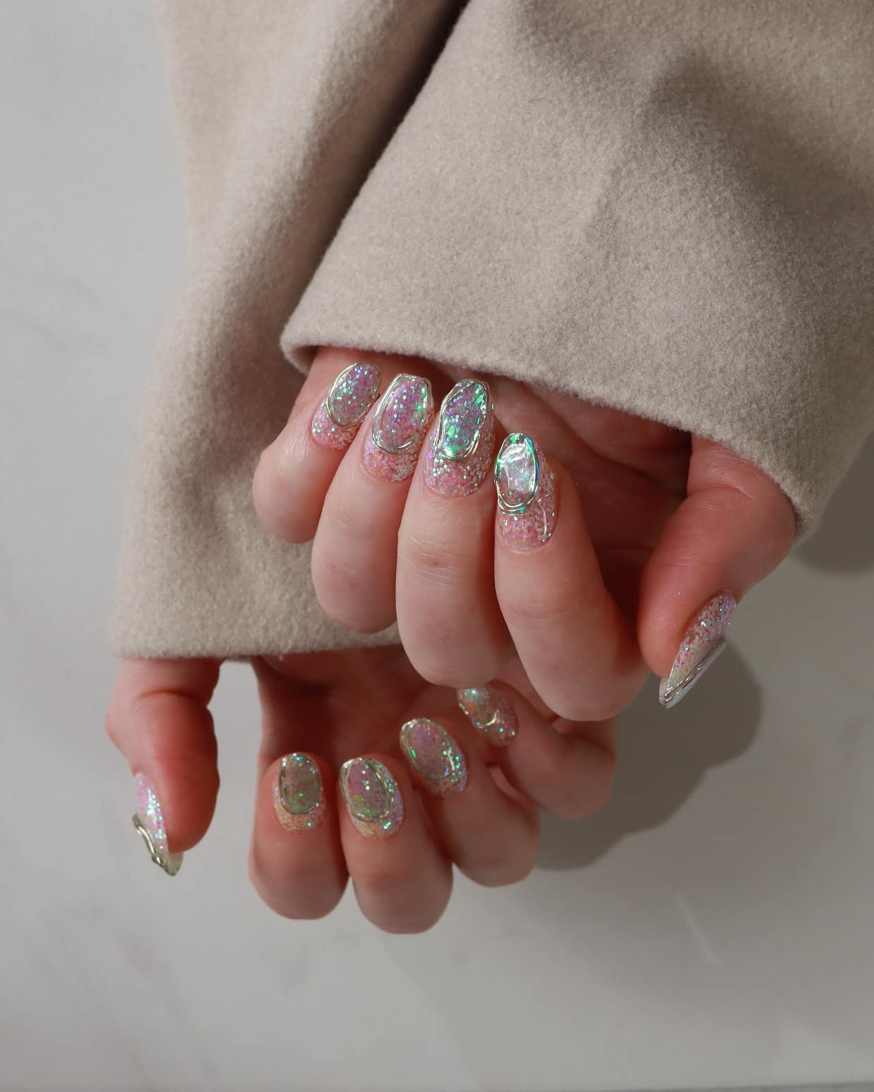 Close-up of hands with glittery nail polish wearing a beige coat.
