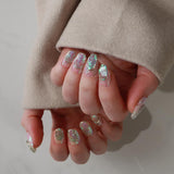 Close-up of hands with glittery nail polish wearing a beige coat.