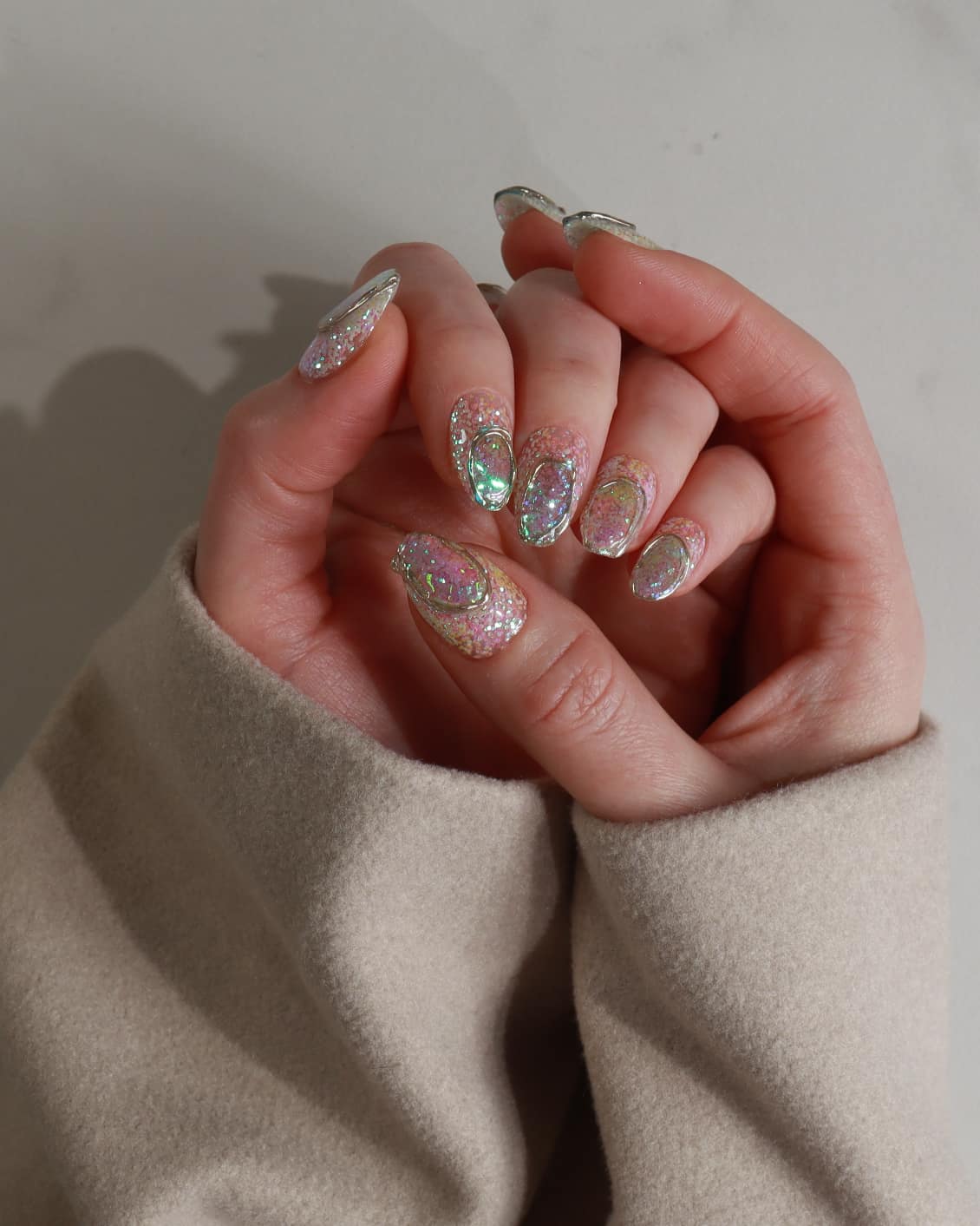 Close-up of a hand with glittery nail polish wearing a beige sleeve.