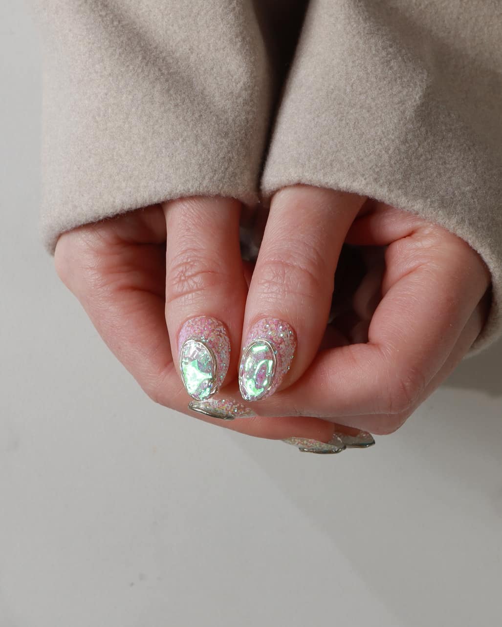 Close-up of hands with decorative nails wearing a beige coat on a neutral background