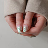 Close-up of hands with decorative nails wearing a beige coat on a neutral background
