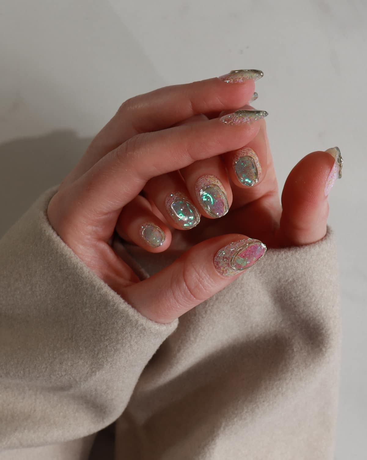 Close-up of a hand with glittery nail polish wearing a beige sweater.