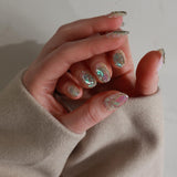 Close-up of a hand with glittery nail polish wearing a beige sweater.