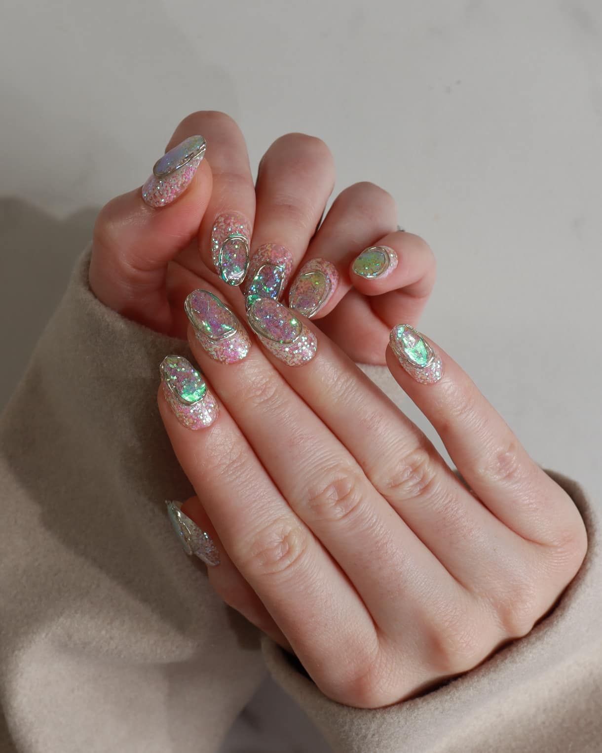 Hand with glittery nail polish on a neutral background