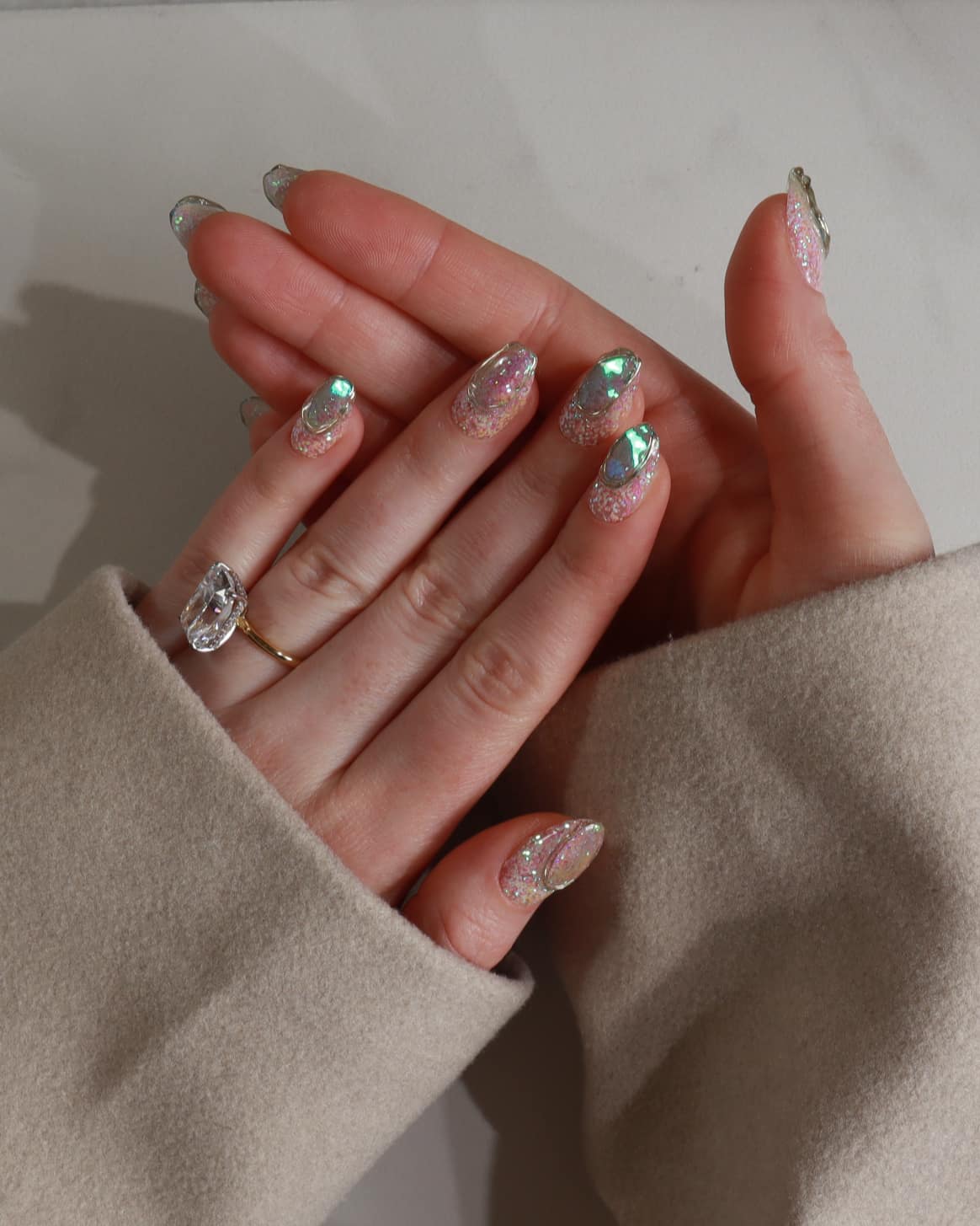 Close-up of a hand with decorative nails and a beige sleeve.