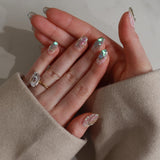 Close-up of a hand with decorative nails and a beige sleeve.