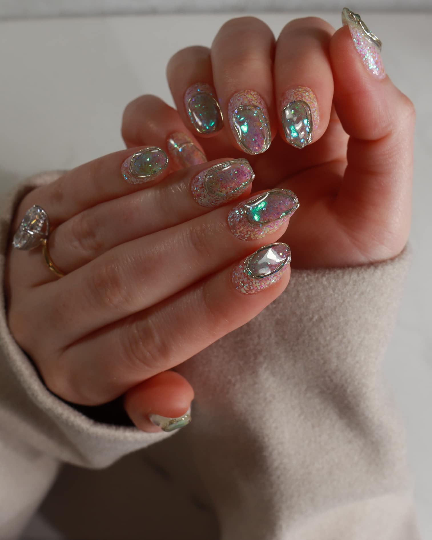 Close-up of a hand with decorative nail art and rings on a neutral background