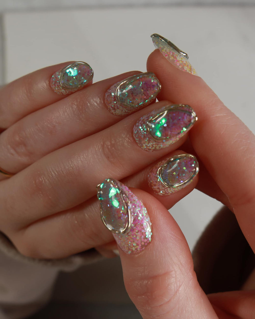 Close-up of a hand with glittery, multicolored nail polish on a neutral background