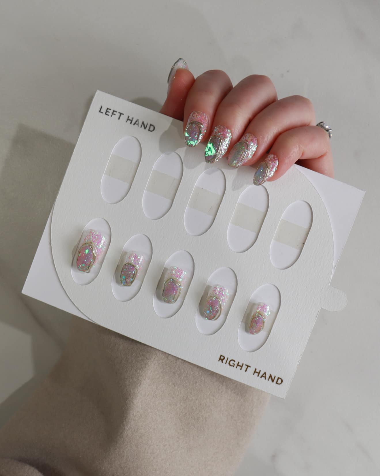 Set of false nails with glittery designs on a display card, held by a hand.