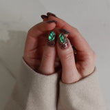 Hand wearing a ring with green gemstone against a neutral background