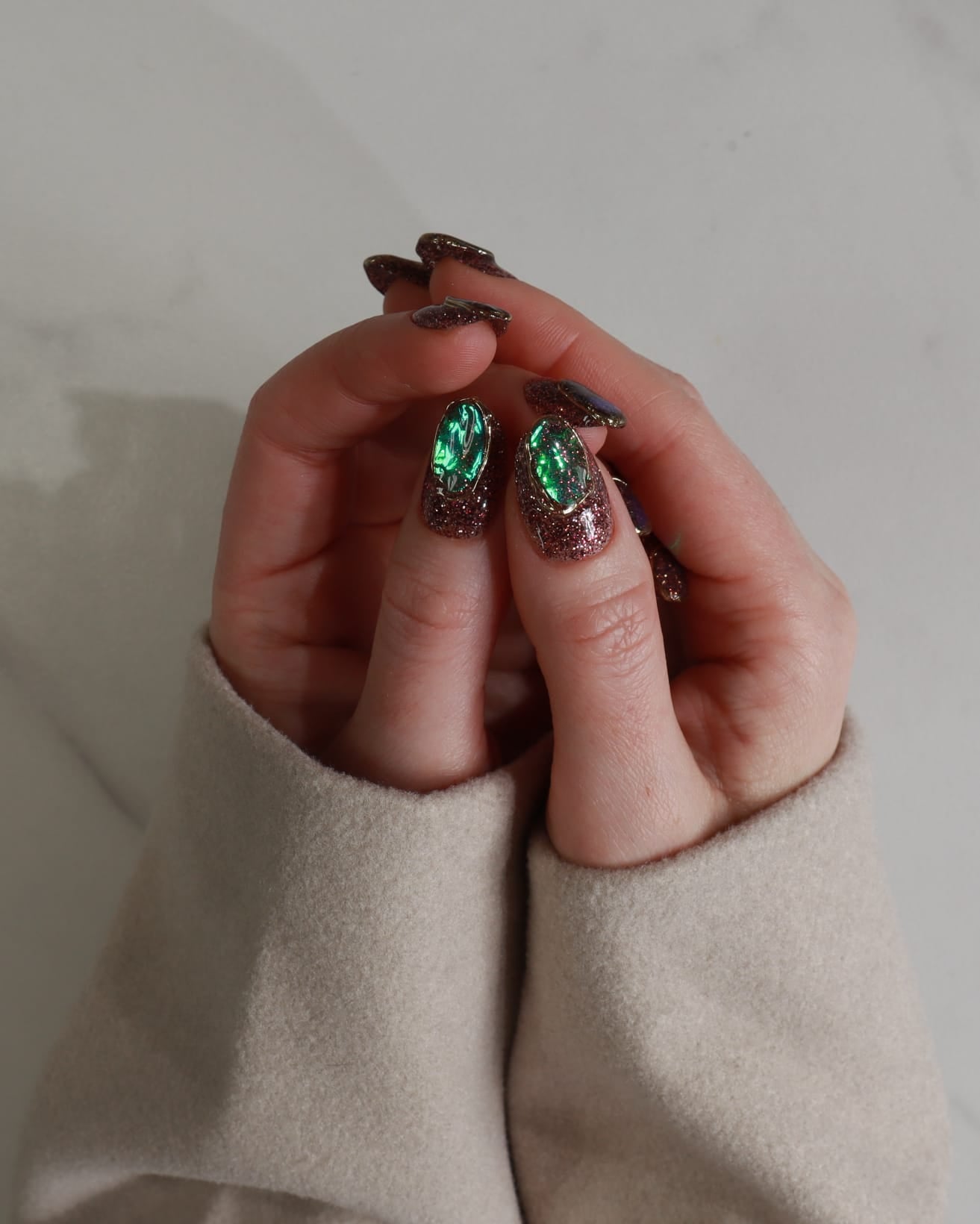 Hand wearing a ring with green gemstone against a neutral background
